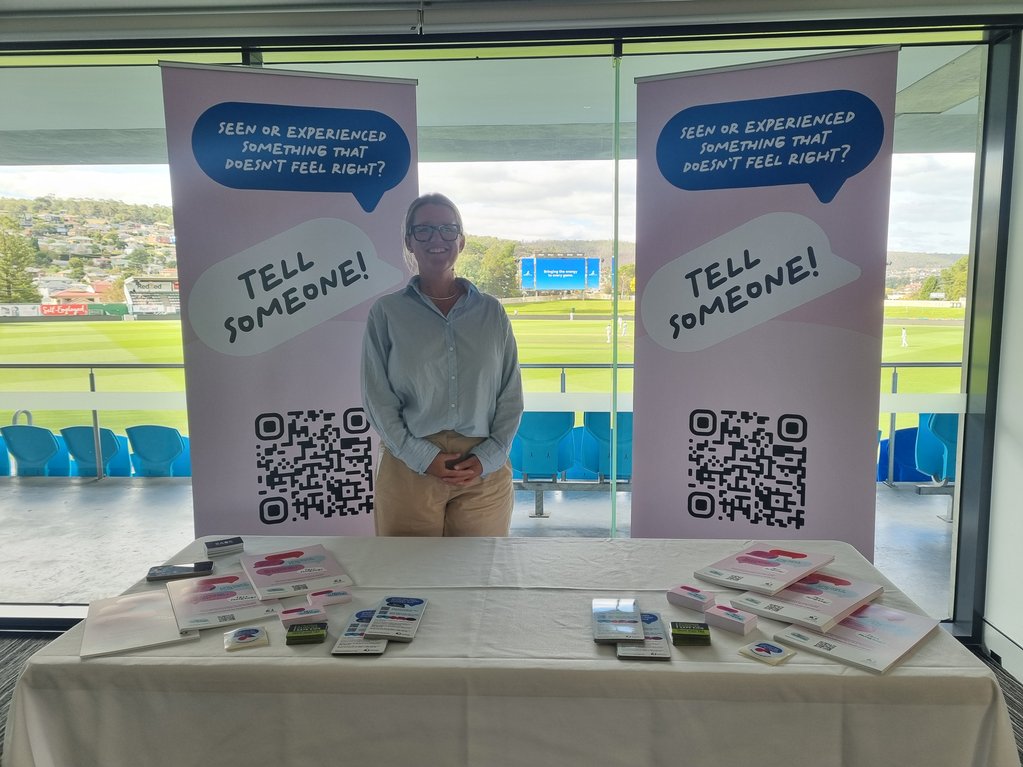a woman standing behind a table next to two banners that read 'Tell Someone'