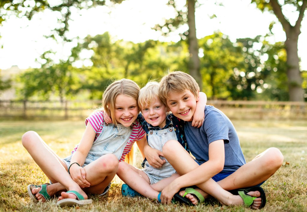 Three smiling children sitting on some grass in a park