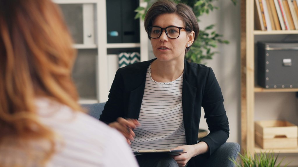 woman wearing glasses holding a clipboard talking with another woman
